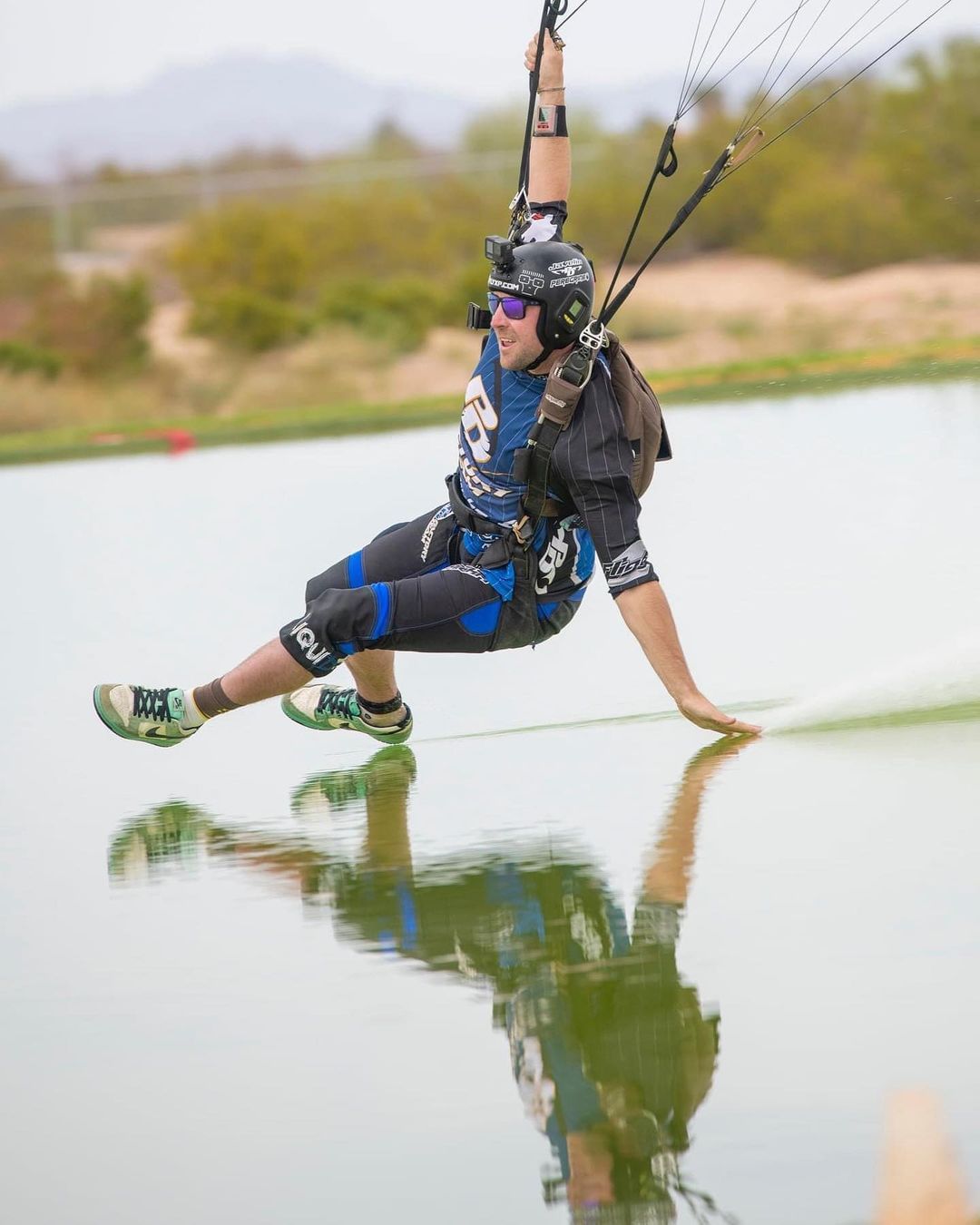 Skydiver wearing a Cookie helmet black and blue jumpsuit swooping over water