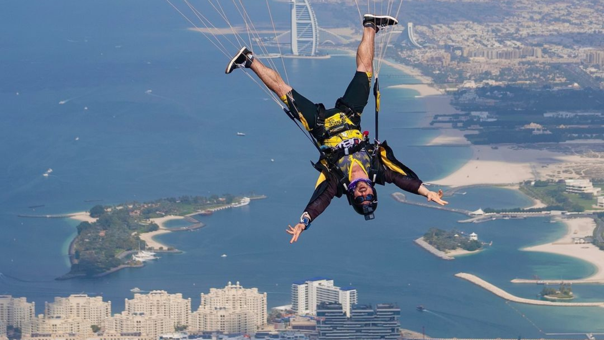 Man in black and yellow jumpsuit flying head down under canopy